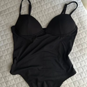 Svart body med kupor - Säljer en svart body med formade kupor. Toppens axelband är smala och justerbara, vilket gör den enkel att anpassa. Skriv till mig om ni är intresserade av att köpa