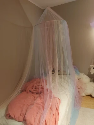 Regnbågsfärgad sänghimmel i nät - Säljer en hel och fin rund sänghimmel i tunt nätmaterial med färger som rosa, blå, lila och gul. Hängs enkelt upp i taket. Köpt från Amazon märke Wnqou. Sängen på bilden är 90×200 cm. 