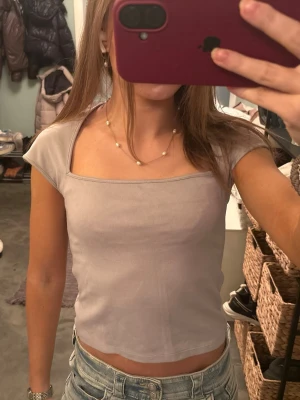 Grå croppad topp från H&M Divided - Säljer en grå croppad topp från H&M Divided i storlek S. Toppen har en fyrkantig halsringning och är kortärmad med en slim passform. Perfekt att matcha med jeans eller kjol för en chill look.( den ser lilla ut med den e grå)