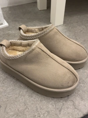 Beige Uggs - Säljer ett par helt nya och oanvända beige boots i storlek 36/37 med platt sula och plattform. Utsidan är i mocka och insidan är fodrad med mjuk fuskpäls. Skorna har rund tå och dekorativt zigzag-mönster runt öppningen. Perfekta för kalla dagar och riktigt mysiga att ha på sig. De är tyvärr lite försmå för mig. Och jag har bara tagit bort lager157 lappen somnär inuti, och de gjorde jag innan jag testade skorna.