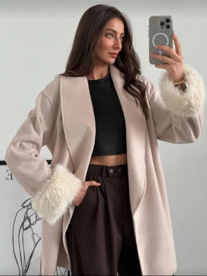 Beige kappa med fuskpälsdetaljer - Säljer en beige kappa med fluffiga fuskpälsdetaljer vid ärmsluten och knytband i midjan. Jackan har en loose passform och är perfekt för dig som gillar en stilren men ändå trendig look. Materialet är mjukt och kappan har en omlottstil som ger en chill vibe.