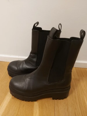 H&M Svarta chelsea boots storlek 38 - Säljer ett par svarta chelsea boots från Divided i storlek 38 i mycket bra skick. Elastiskt tyg på sidorna. Praktiska dragflikar upptill för enkel påtagning.