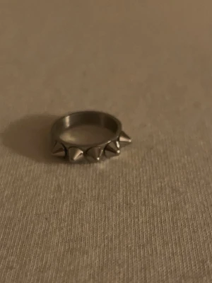 Silvrig ring med nitar - Cool silvrig ring med små nitar runt hela bandet. Ringen har en edgy vibe och passar perfekt om du gillar att sticka ut med din stil. Metallfinishen ger en snygg och modern känsla. Perfekt accessoar för att ge din outfit lite extra attityd.