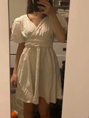 Vit klänning - Säljer en söt vit kortklänning med omlottdesign och puffiga kortärmar. Klänningen har markerad midja.