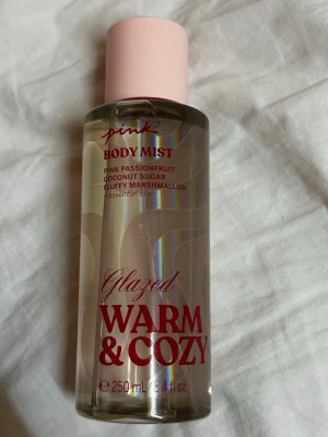 Pink Glazed Warm & Cozy Body Mist - Body mist med pink passionfruit, coconut sugar och fluffy marshmallow samt essentiella oljor. Volym: 250 ml. Perfekt för dig som vill ha en fräsch och söt touch i din vardag.