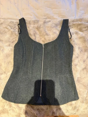 Grå korsett-topp från Zara - Snygg grå korsett-topp från Zara i storlek M. Toppen har en markerad siluett, breda axelband och en silverfärgad dragkedja framtill. Materialet är mjukt och känns som en blandning av bomull och syntet. Perfekt att styla med jeans eller kjol. Pris kan diskuteras!!💖