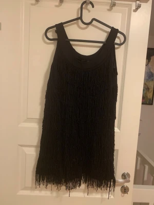 Svart fransklänning från H&M - Säljer en svart kortklänning från H&M i storlek S. Klänningen har flera lager med fransar som ger en cool och livlig look. Ärmlös modell med rund halsringning, perfekt för dig som gillar att sticka ut. Materialet är mjukt och bekvämt.