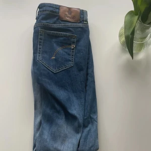Blå jeans från Dondup, storlek 30 (28, tighta) - Snygga blå jeans från Dondup i klassisk femficksmodell. Jeansen har en rak passform och är tillverkade i en mjuk bomullsblandning med lite stretch. Fina kontrastsömmar och läderpatch med logga bak i midjan. Made in Italy skriv om du har funderingar. Obs: tighta i modellen, mer som 28.. Kolla bilder för mått samt design i ena byxbenet med slitet längst ner.