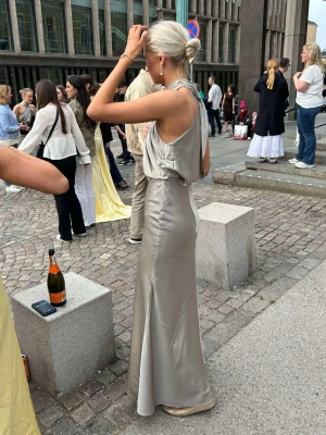 Champagnefärgad/olivgrön långklänning i satin - Supersnygg långklänning i champagnefärgad/ salvia- olivgrön satin med omlott-drapering upptill och halterneck. Klänningen har en slits och en figurnära passform! Perfekt för bal❣️ Säljes då jag köpte den för min bal 2025☺️ skriv för bättre bilder på klänningen eller frågor. NY PRIS 1569 kr