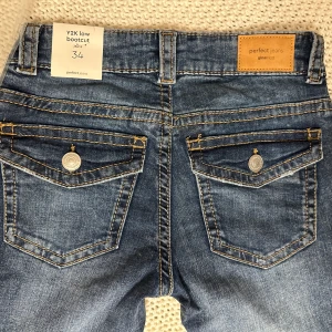 Y2K low bootcut jeans Gina Tricot - Snygga blå lågmidjade bootcut jeans från Gina Tricot med klassiska fickor med lock bak. Jeansen har en autentisk Y2K-vibe, kontrastsömmar. Väldigt sköna med stretch, helt nya med lapparna kvar, köpta för 500kr 