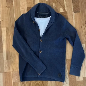 Blå kofta från Marc O'Polo i bomull - Snygg blå kofta från Marc O'Polo i bomullsmaterial. Koftan har ribbade muddar, knappar framtill och en cool logodetalj nertill. Perfekt för lager-på-lager och chill stil. Skön passform och långärmad modell. Säljer pågrund av att den inte passar mig längre. Priset är ej hugget i sten🙌✌️