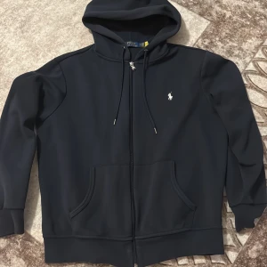 Mörk blå Ralph lauren zip hoodie - En mörk blå Ralph lauren zip hoodie i super bra skick, har haft på mig den ett par gånger men passar inte jätte bra. Storlek M men passar även storlek S. Hör av er om ni är intresserad😊