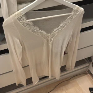 Krämvit blus med spets från Intimissimi - Superfin krämvit blus från Intimissimi i mjuk kashmirblandning. V-ringad med spetsdetaljer runt halsringning och ärmslut. Långärmad och tunn, perfekt för lager-på-lager. Snygg och feminin look med lyxig känsla. Oanvänd 