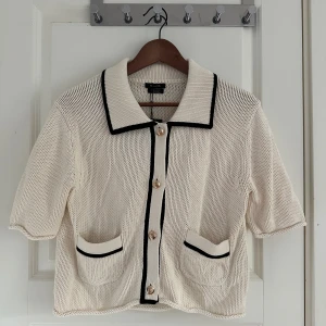 Beige kofta från Massimo Dutti - Superfin beige stickad kofta från Massimo Dutti i 100% bomull. Kortärmad modell med svarta kontrastkanter, dekorativa fickor framtill och snygga guldknappar. Oanvänd 🫶🏽