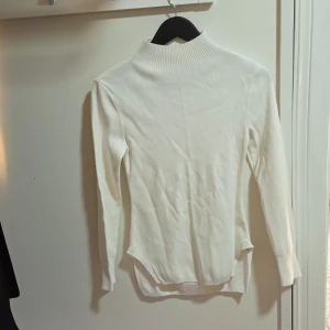 Vit polotröja med öppen rygg från Zara - Säljer en vit polotröja från Zara med lång ärm och ribbad krage. Tröjan har en snygg öppen rygg med två knytband som ger en unik look. Perfekt för dig som vill sticka ut med en stilren men ändå speciell tröja.