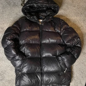 Zara puffer jacket - Säljer en svart pufferjacka från Zara i storlek S. Jackan har en stor huva, dragkedja framtill och två fickor med dragkedja. Perfekt för kalla dagar och har en riktigt fet, oversized look. Materialet är glansigt och känns lätt men ändå varmt.