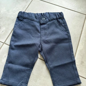 Mörkblå rutiga byxor från H&M 68 - Mörkblå byxor från H&M i storlek 68 med rutigt mönster. Byxorna har elastisk midja, knapp framtill och fickor både fram och bak. Perfekta för en stilren look till de minsta.
