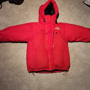 Röd dunjacka The North Face Summit - Riktigt fet röd dunjacka från The North Face Summit Series. Jackan har huva, flera dragkedjor och logga på bröstet och ärmen. Perfekt för kalla dagar och har en schysst oversized vibe. Innerfodret är svart och jackan har justerbara snören nertill. Dessa jackor är väldigt eftertraktade eftersom dom inte görs mer!