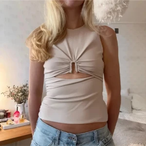 Beige croppad linnetopp  - Säljer en beige croppad linnetopp med snygg snörning och cut-out framtill. Toppen är ärmlös och har en tight passform som framhäver midjan. Materialet känns mjukt och  perfekt för dig som gillar trendiga detaljer och stilren look.