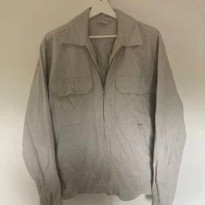 Ljusbeige overshirt från Yoke - Säljer en stilren ljusbeige overshirt från Yoke i manchester. Skjortan har två stora bröstfickor med lock, klassisk krage och dragkedja framtill. Perfekt lager-på-lager plagg till hösten. Storlek M men passar dig som är runt 185.