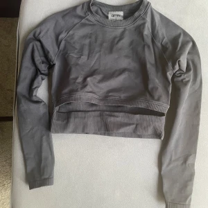 Mörkgrå croppad sweatshirt Aim'n - Ljuset kan få den att se grå ut men den är tydligt svart - croppad sweatshirt från Aim'n. Tröjan har långa ärmar, bred ribbad mudd i midjan och vid ärmslut samt rund halsringning. Perfekt för en chill och sportig look.