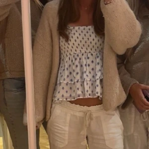 Vit blommig volangtopp - Supersöt vit topp med blått blommönster och volanger. Axelbandslös bandeau-modell som är perfekt för varma dagar. Toppens material känns lätt och luftigt, och den har en croppad passform som ger en trendig look.