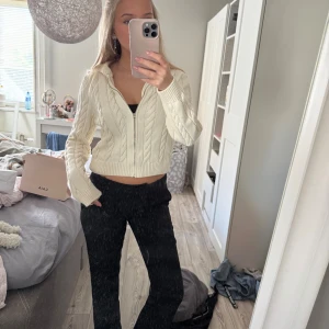 Vit stickad hoodie med dragkedja - Superfin vit stickad hoodie med dragkedja framtill och snygg kabelstickad design. Croppad modell med huva och långa ärmar, perfekt till jeans eller kjol. Ribbade muddar och mjukt material som känns skönt mot huden. Sitter bra på s