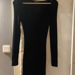 Svart ribbad långärmad klänning - En svart, tight ribbad klänning  med lång ärm. Klänningen är kort och har en stilren, minimalistisk look som passar perfekt när du vill känna dig extra snygg.