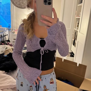 Ljuslila stickad bolerotopp med knyt - Superfin ljuslila bolerotopp i stickat material med långärmad design och snygg knytning framtill. Toppen har ett öppet hål vid bröstet och ett coolt mönster i stickningen. Perfekt att slänga över en enkel topp för att få en extra touch till outfiten.