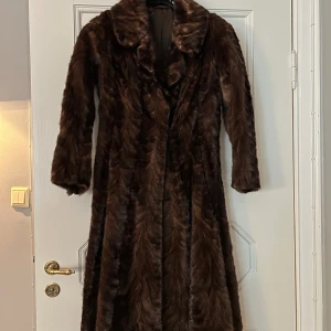 Lång brun pälsjacka med krage - Säljer en lång och lyxig brun pälsjacka med bred krage och helknäppning. Jackan har en klassisk siluett och är helfodrad på insidan. Perfekt för dig som vill sticka ut och hålla dig varm under kalla dagar.