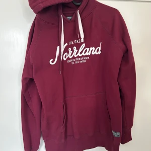 Vinröd hoodie The Great Norrland - Säljer en vinröd hoodie från The Great Norrland med vit text på bröstet och klassisk känguruficka. Tröjan har huva med snörning och långa ärmar. Perfekt för dig som gillar en avslappnad och snygg stil. Använd vid ca 2 tillfällen, som ny.