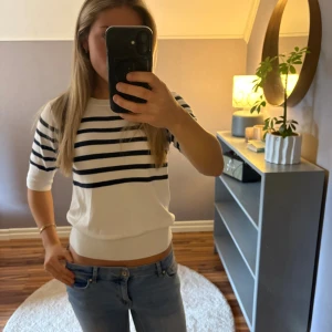 Vit och marinblå randig tröja - Säljer en fräsch vit tröja med marinblå horisontella ränder över bröstet och ärmarna. Tröjan har rund hals och trekvartsärm, samt en bred ribbad kant nedtill. Perfekt för dig som gillar klassisk och stilren look.