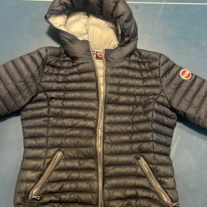 Mörkblå pufferjacka från Colmar - Snygg mörkblå pufferjacka från Colmar med huva och två dragkedjeförsedda fickor. Jackan har quiltad design och Colmar-logga på ärmen. Perfekt för kyliga dagar och riktigt skön att bära.