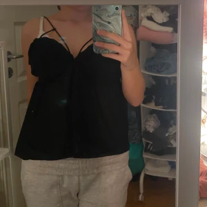 Svart fest topp med öppen rygg - Säljer en svart festtopp, as snygg men tyvärr för stor. Axelband och snygg omlottkänsla framtill. Toppen har öppen rygg med knytband💗