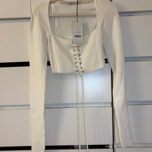 Vit croppad topp med snörning NAKD - Säljer en vit croppad topp från NA-KD med långa ärmar och snygg snörning framtill. Toppen har fyrkantig urringning.