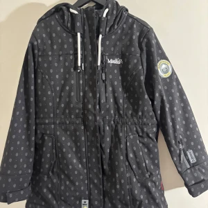 Svart mönstrad jacka  - Svart vindjacka med grått prickigt mönster, huva med dragsko och flera dragkedjeförsedda fickor. Jackan har lång ärm, justerbar midja och är fodrad med mjukt material på insidan. Perfekt för kyliga dagar och outdoor vibes.