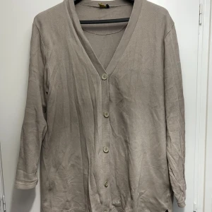 Beige kofta med knappar och v-ringning - Beige kofta från Spade med v-ringad hals och knäppning framtill. Modellen har trekvartsärm och är tillverkad i mjuk bomull. Perfekt för lager-på-lager och enkel att matcha med andra plagg.