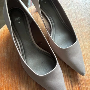 Zara klackar - Klackar från Zara, köpta i vintras för ca 500 kr. Använda men ändå i fint skick, allt syns på bilderna som är tecken på användning. Glansigt satin liknande material, ascoola. Beige-grå i färgen