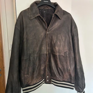 Brun skinn bomberjacka från ASOS Design - Säljer en brun bomberjacka i skinn från ASOS Design. Jackan har klassisk krage, tryckknappar framtill och ribbade muddar med svartvita ränder. Perfekt oversized passform och två fickor framtill. Snygg vintagekänsla och riktigt cool look. Slutsåld.