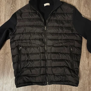 Svart dunväst från Moncler, storlek L (Intresse bara ska inte sälja den nu) - Svart dunväst från Moncler i storlek L med quiltad design och två dragkedjeförsedda fickor framtill. Västen har en stilren look med ståkrage och hel dragkedja. Materialet är polyester och dun, perfekt för kyliga dagar. Märket syns på insidan och etiketten. (Intresse bara ska inte sälja den nu), till ett bra pris kan kompromissa.