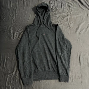 Mörkgrå hoodie från Tommy Jeans - Snygg mörkgrå hoodie från Tommy Jeans med broderad logga på bröstet. Haft på mig några gånger, älskar den men Tommy är inte min stil. Skick är bra som ny och den är nog den skönaste hoodien jag har haft.