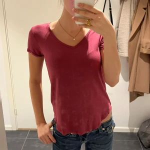 Vinröd v-ringad t-shirt - Säljer en enkel och snygg vinröd t-shirt med v-ringning och korta ärmar. Modellen är normal i passformen och tillverkad i mjuk bomull som känns skön mot huden. Perfekt att matcha med jeans eller shorts för en chill look.