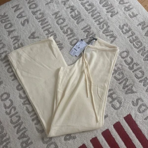 Vaniljgula stickade byxor Gina Tricot - Mjuka stickade byxor från Gina Tricot i en ljus vaniljgul färg. Byxorna har dragsko i midjan och raka, vida ben för en chill och avslappnad look. Perfekta att matcha med en hoodie eller crop top för en trendig vibe.