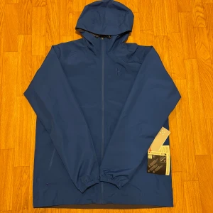 Blå vindjacka från Haglöfs GTX II - Säljer en blå vindjacka från Haglöfs, modell Chaos GTX II. Jackan har huva, hel dragkedja framtill och elastiska muddar vid ärmslut. Insidan är fodrad med mesh för extra ventilation. Perfekt för dig som gillar stilren och funktionell design.