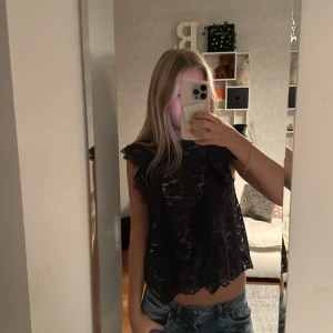 Mörkblå spetsblus med volangdetaljer - Säljer en mörkblå blus i spets med fina volangdetaljer vid axlarna och ärmlös design. Blusen har hög hals och ett genombrutet mönster som ger en cool och elegant look. Perfekt att styla med jeans eller tight kjol❣️❣️