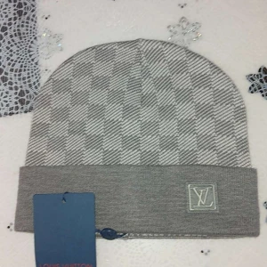 Grå rutig mössa  - Snygg grå mössa med klassiskt rutigt mönster och vikt kant.  broderad framtill. Tillverkad i mjukt stickat material som håller dig varm och stilren under kalla dagar. Perfekt accessoar för dig som gillar exklusiva detaljer.