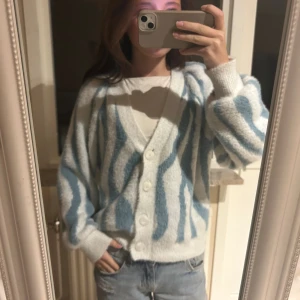 Unik jätte söt kofta vila  - Mysig och fluffig kofta med zebramönster i ljusblått och vitt. Koftan har v-ringning, stora vita knappar framtill och långa ärmar med breda muddar. Passformen är loose och materialet känns stickat och mjukt, perfekt för att ge en chill vibe.