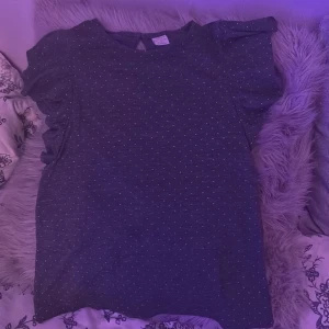 Mörkblå prickig t-shirt från Lindex - Kan säka priset om de önskas!!!Mörkblå t-shirt från Lindex med små vita prickar över hela tyget. T-shirten har korta ärmar och en söt knappdetalj i nacken. Perfekt för dig som gillar en enkel men ändå söt stil.