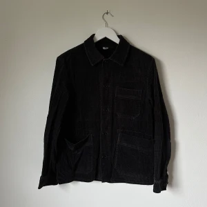 Mörkgrå manchester overshirt från ARKET - Mörkgrå overshirt från ARKET i mjuk manchester med klassisk krage, stora fickor fram och knäppning med knappar. Perfekt att slänga på över en t-shirt för en chill look. Materialet är bomullsblandning och modellen är långärmad. 4E1