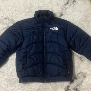 Mörkblå pufferjacka från The North Face - Säljer en mörkblå pufferjacka från The North Face i storlek M.Perfekt för kalla dagar med sin quiltade design och snygga passform. Anledingen till varför jag säljer den är då att jag har köpt en ny jacka o har ingen behov längre av denhär, den är nästan nyskick och har nästan inga täcken på användning